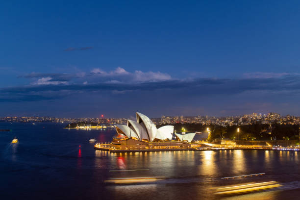 Sydney, Australia - The Sydney Opera House illuminated at dusk, with the light reflecting in the water of Sydney Harbour.