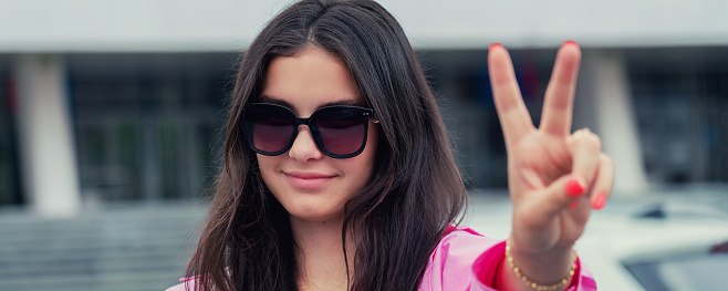 Young woman wearing sunglasses showing victory sign close view outside