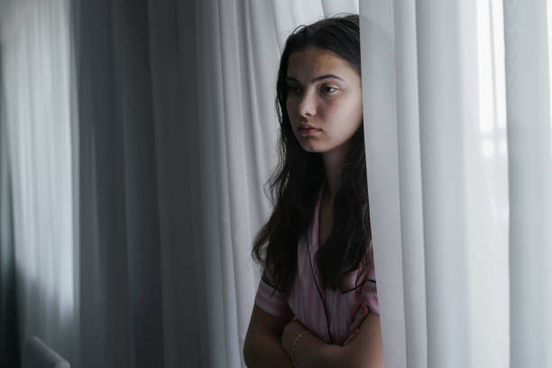 adolescente infeliz sola parada en casa contra la ventana - teenager adolescence portrait pensive fotografías e imágenes de stock