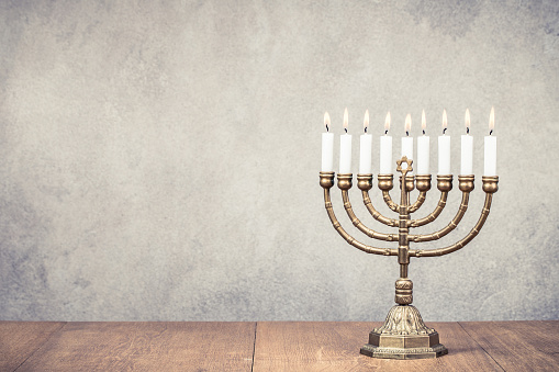 Bronze Hanukkah menorah with burning candles on wooden table front old vintage concrete wall background. Holiday greeting card concept. Retro style filtered photo