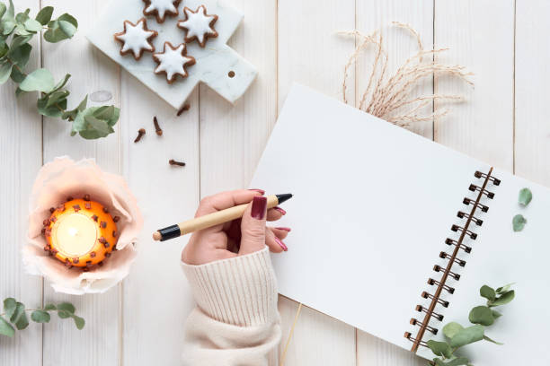 istock Wintertime notebook mockup with eucalyptus twigs, natural orange tea light with cloves and gingerbread cookies on ceramic board. Flat lay, top view on off white rustic wooden ff white planks. 1437102470