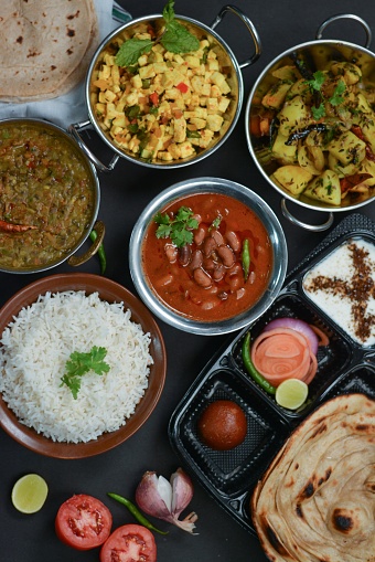 Indian food flatlay which contains rice, thali, rajma,dal ,paneer, chapati,curd and gulab jamun.