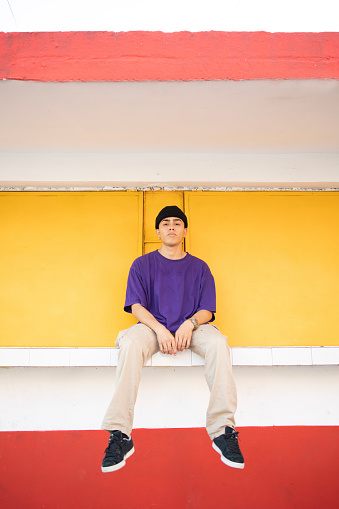 Portrait of a young Mexican man looking at the camera. He is wearing purple shirt on a colorful background