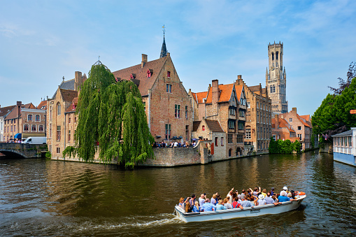 Bruges, Belgium - May 29, 2018: Tourist boat passin in famous Bruges tourist landmark - Rozenhoedkaai canal with Belfry and old houses along canal