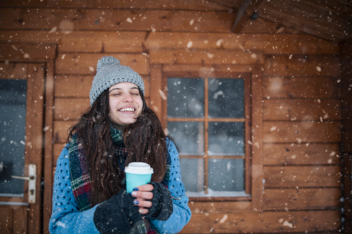 Young woman on the porch drinking a hot drink and enjoying the beautiful winter in the mountains.
