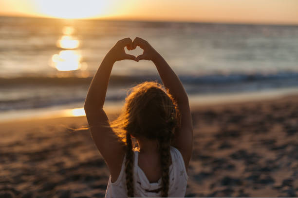 Girl making heart with her hand on the beach on sunset. High quality photo