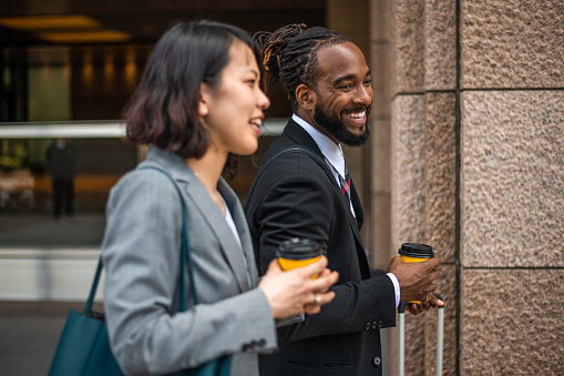Male and female professional accountants and colleagues meet to buy coffee before going to the office. They are talking and smiling while walking on their way to work. They are wearing formal businesswear.