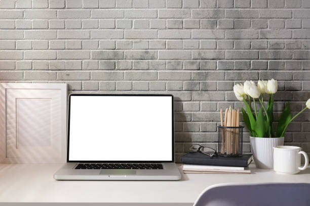 istock Front view computer laptop with empty display, books and potted plant on white table. 1437136740