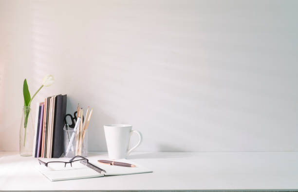 istock Minimal workplace with coffee cup pencil holder notebook and flower pot on white table. Copy space for your advertise text. 1437136852