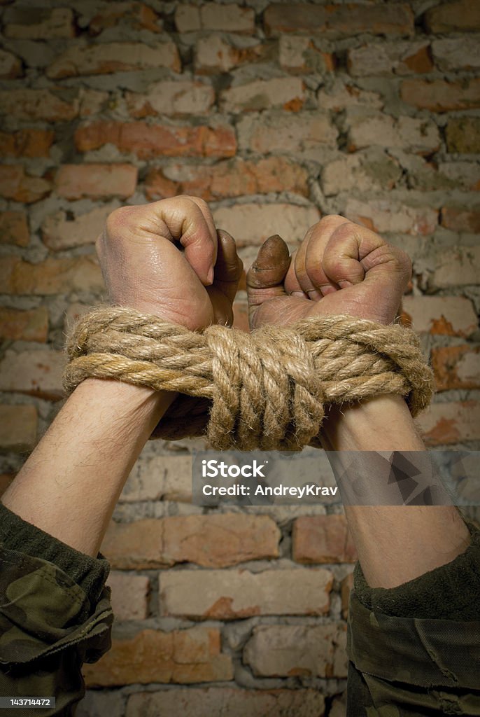 Hands tied up with rope Hands tied up with rope against brick wall Brick Wall Stock Photo