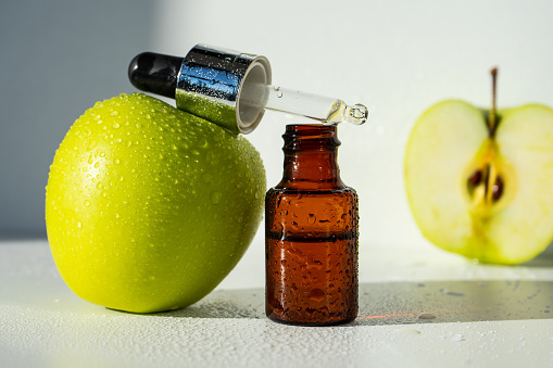 A bottle of apple essential oil and an eyedropper on a white table. Apple butter. Essential oil is used for refueling lamps, perfumes and cosmetics. Close-up. Selective focus.