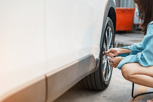 woman driver hand inflating tires of vehicle, removing tire valve nitrogen cap for checking air pressure and filling air on car wheel at gas station. self service, maintenance and safety