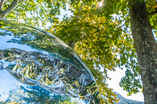 Chrome sphere reflecting trees and blue sky. Lugano. Switzerland. Canton Ticino. High-quality photo