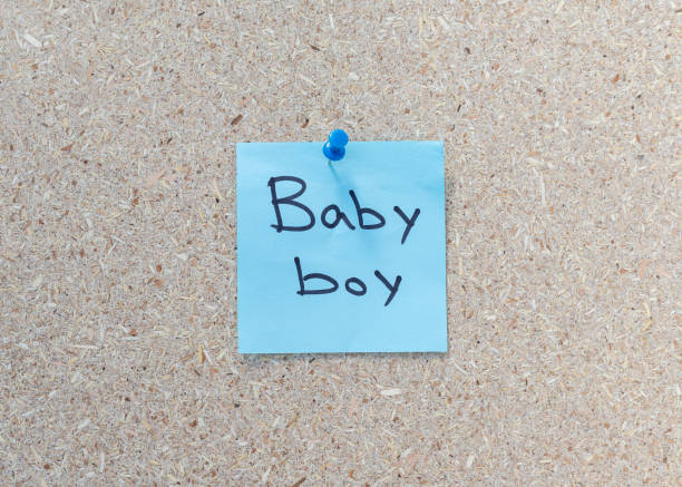 Surprise gender reveals hand written message on a a blue sticky note on a corkboard background with copy space