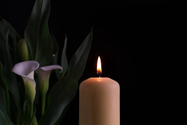 Candle burning flame in the darkness and arum lilies stock photo