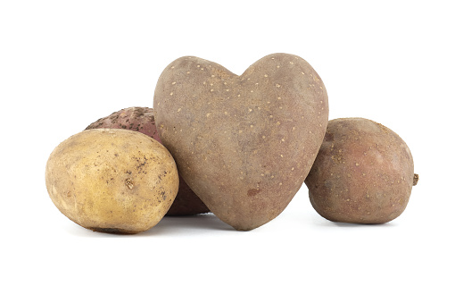 Heart-shaped potato in front of a pile of multicolored potatoes over a white background