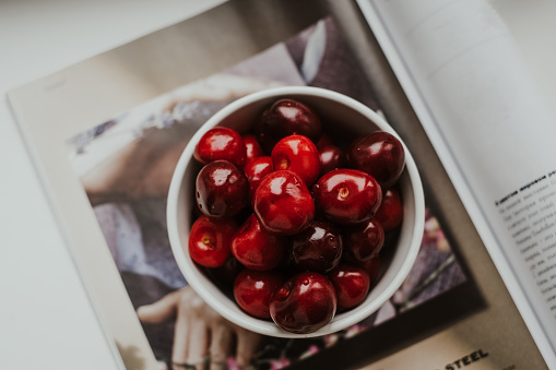 Sweet cherries in a white bowl standing on a magazine cover.