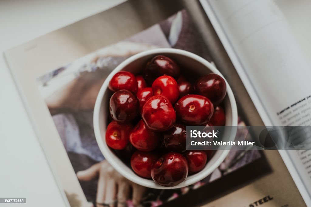 Sweet cherries in a white bowl standing on a magazine cover. Berry fruit season. Fresh sweet cherries. Cherry Stock Photo