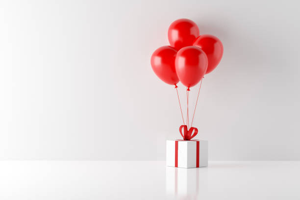 istock White gift box with red ribbon and red helium balloons on white background. Celebration, shopping and buying a surprise present 1437177186