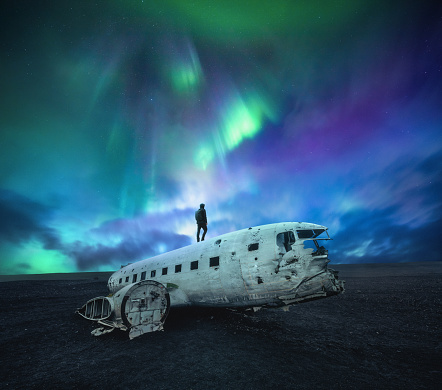 Man standing on top of plane wreck on the black beach at Solheimasandur, in the South coast of Iceland under the northern lights.