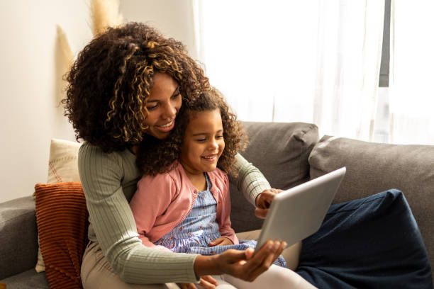 Mother and daughter using digital tablet Mother and daughter sitting in the living room and using digital tablet black mother and adult daughter stock pictures, royalty-free photos & images