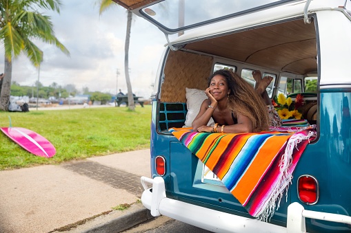 Beautiful black woman lying in Volkswagen van on the beach in Hawaii