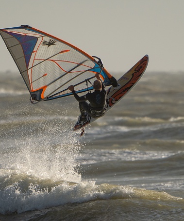 Young girl pulling a sail from the water before windsurfing in a blue ocean in a summertime.