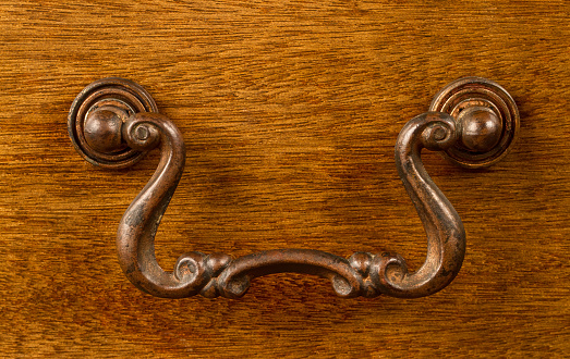 Antique metal handle on a wooden surface. Decorative metal handle of the original shape.