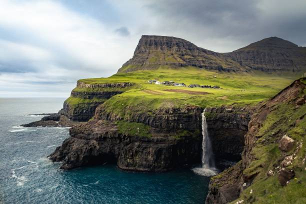 istock Waterfall streams from a green cliff and a small town by the coast 1437183855