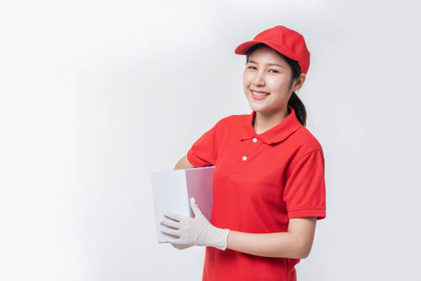 istock Image of  young delivery man in red cap blank t-shirt uniform standing with empty white cardboard box isolated on light gray background studio 1437186056