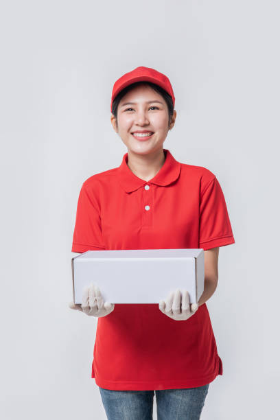 istock Image of  young delivery man in red cap blank t-shirt uniform standing with empty white cardboard box isolated on light gray background studio 1437186096