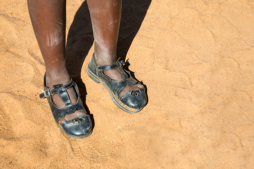African girl broken school shoes in the hot sand walking in the desert