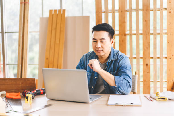 mittelalter erwachsener asiatischer mann tischler mit laptop für online-arbeit mit kunden wotk zu hause - southeast asian ethnicity men laptop image type stock-fotos und bilder