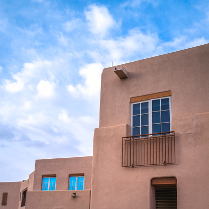 Southwestern Adobe style red stucco building facade wall with windows against blue cloudy sky