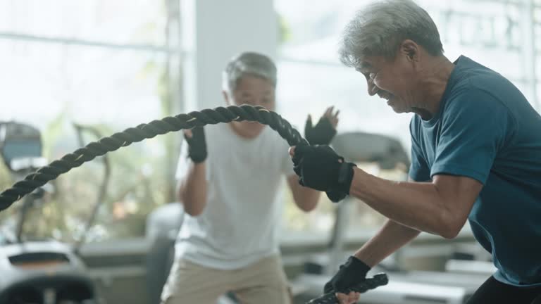 Asian Chinese Senior personal trainer encouraging senior man practicing battle rope in gym