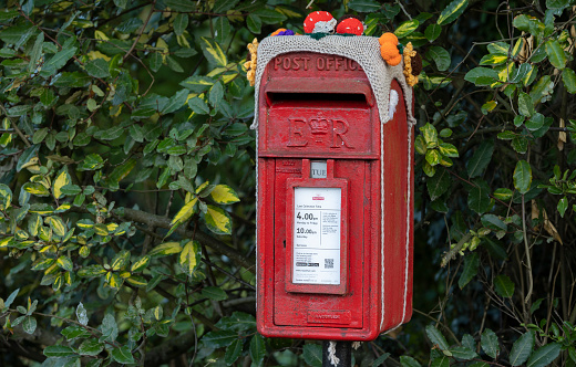 Traditional British red Royal Mail mailbox with decorations on top, local traditions