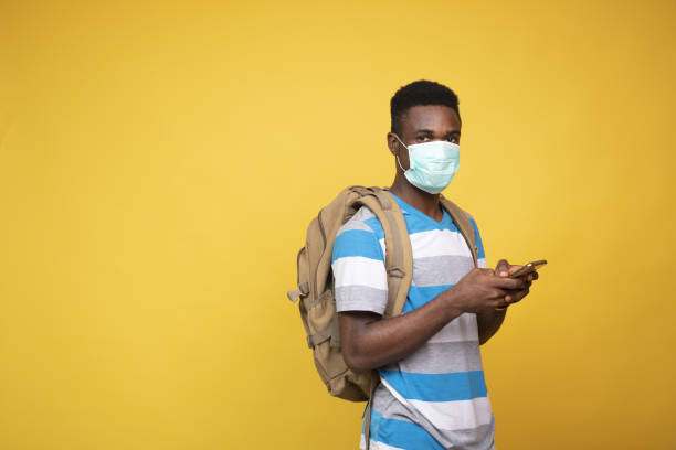 istock African male with a backpack wearing a facemask and using his phone against a yellow background 1437197967