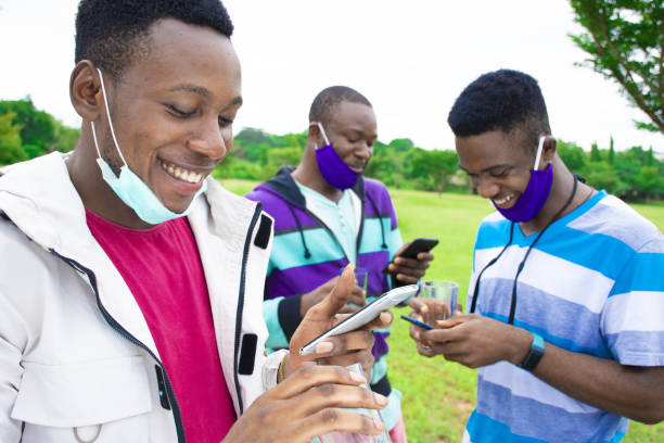 istock Group of young African friends with facemasks using phones while social distancing in a park 1437198403