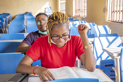 A shallow focus of two young African students wearing facemasks and studying in a classroom