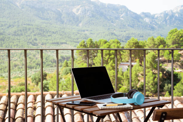 istock Laptop, blue headsets, a notebook, and a cellphone on the table on a balcony with a beautiful view 1437199685