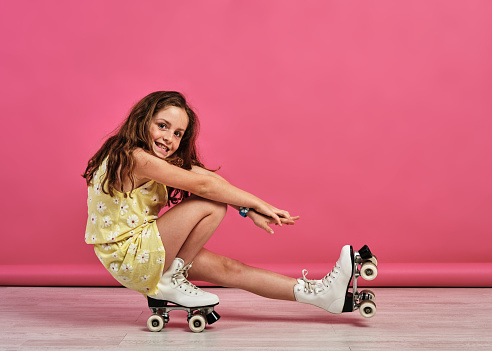 A little girl doing tricks with roller-skates in a studio with a pink background