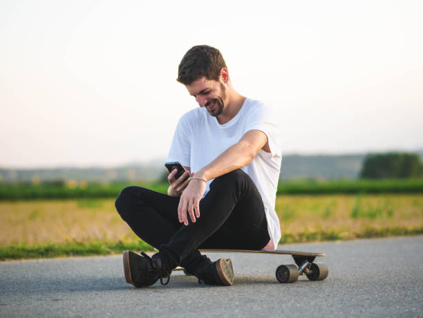 istock Young handsome male sitting on a skateboard and using a smartphone 1437201916