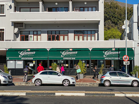 Cape Town, South Africa – May 12, 2020: Customers standing in queue observing social distancing guidelines while waiting to enter Giovanni's deli on a Sunday morning in Cape Town
