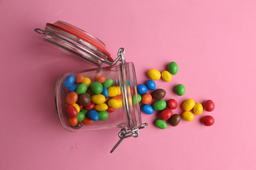 The colorful chocolate balls in a glass jar on a pink background