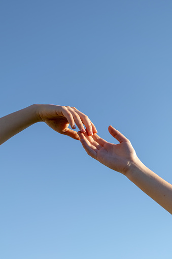 A vertical shot of two hands reaching out to each other on a blue sky background