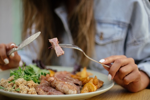 A selective focus shot of a female eating a dish with steak and potato