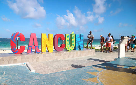 Cancun, Yucatan, Mexico – July 19, 2019: Tourists pose for photos next to the colorful Cancun sign along the beach.