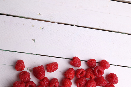A high angle shot of some fresh and delicious raspberries isolated on a white wooden surface