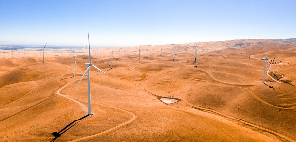 A high angle shot of the wind turbines in a sandy field captured on a sunny day