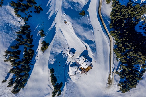 An overhead shot of small houses on a snowy mountain surrounded by trees during daylight